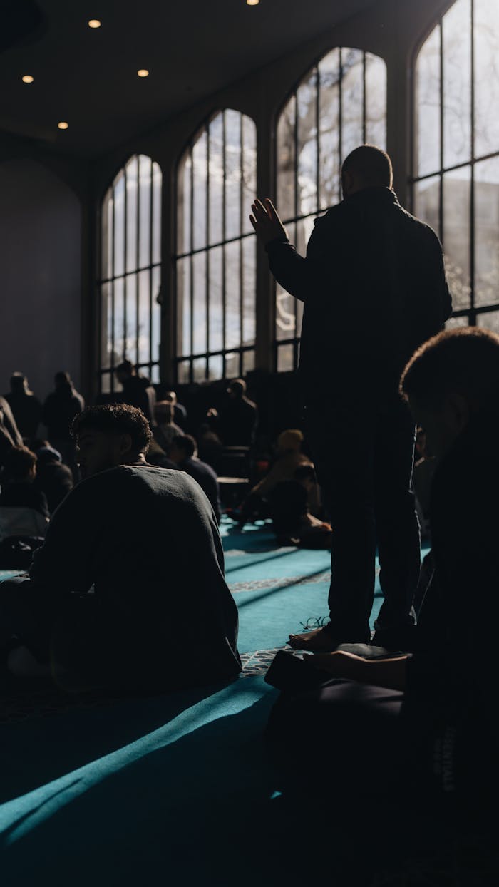 Silhouetted individuals praying inside a mosque, casting dramatic shadows.