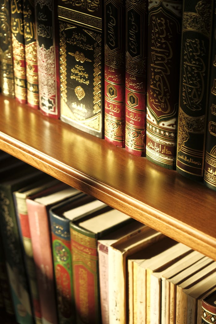 Beautifully ornate religious texts on a wooden bookshelf illuminated by gentle sunlight.
