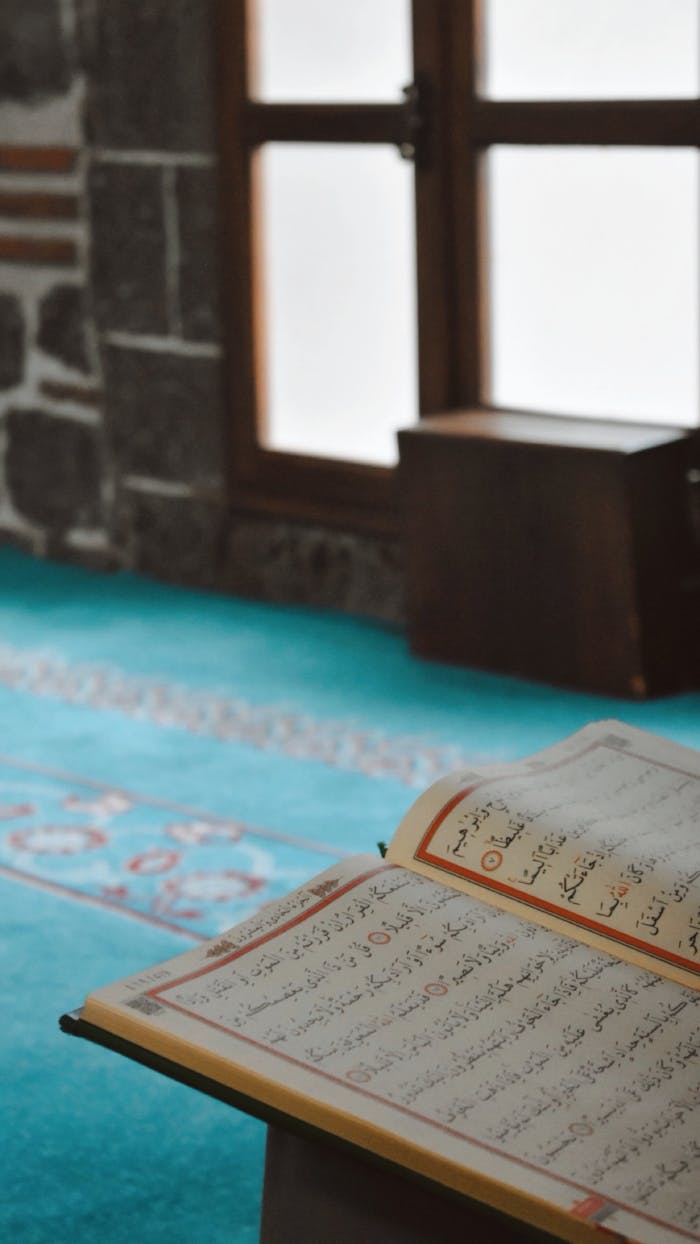 An open Quran inside a calm and serene mosque interior with turquoise carpet.